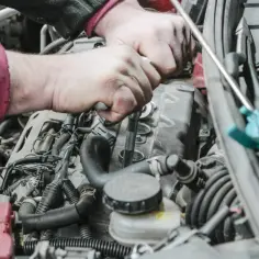 Ręce mechanika dokonują wymiany świec zapłonowych w silniku samochodu, używając klucza nasadowego.