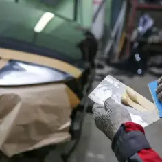 Ręce w rękawicach nakładają szpachlę samochodową na element auta. Czas schnięcia szpachli zależy od warunków.