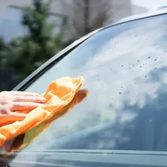 Ręka z pomarańczową ściereczką czyści szybę, pokazując, jak usunąć naklejkę z szyby.