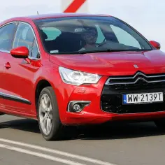 Czerwony Citroen DS4 w ruchu drogowym. Kierowca w okularach. Wiele pozytywnych **citroen ds4 opinie** potwierdza jego styl.