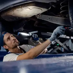 Mechanik z latarką bada podwozie auta, przygotowując się do wymiany tulei wahacza.