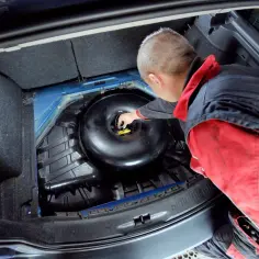 Mechanik dokonuje wymiany butli gazowej w samochodzie, sprawdzając zawór.