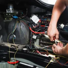 Mechanik naprawia okablowanie w samochodzie. Może to być związane z objawami silniczka krokowego, takimi jak nierówna praca silnika.