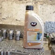 Butelka oleju do skrzyni biegów ATF III K2 na stole z częściami automatycznej skrzyni biegów.