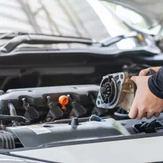 Mechanik wymienia zużyty rozrusznik w samochodzie. Widać jego ręce trzymające element silnika.