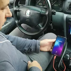 Mężczyzna w samochodzie pokazuje, jak połączyć telefon z autem za pomocą kabla i aplikacji Weblink.