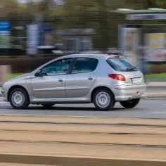 Srebrny Peugeot 206 Plus pędzi po ulicy, rozmywając tło.