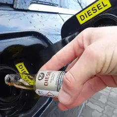 Ręka wlewa dodatek do diesla z małej buteleczki do baku samochodu.