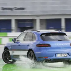 Niebieski Porsche Macan Turbo na mokrym torze, rozpryskuje wodę. Na tylnej szybie numer 27, a na karoserii napis "Driving Center".