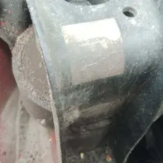 Zużyta poduszka silnika objawy: wibracje, stuki. Widoczny element gumowy z metalowym mocowaniem, pokryty kurzem.
