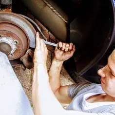 Młody mechanik z brudnymi rękami dokręca śrubę przy kole. Zastanawia się nad wymiana łożyska w kole cena.