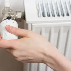 Dłoń reguluje termostat grzejnika.