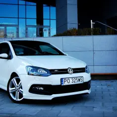 Biały VW Polo 1.2 benzyna z czarnym dachem, zaparkowany przed nowoczesnym budynkiem.