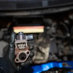 Zardzewiały zawór EGR w dłoni mechanika, gotowy do wymiany w silniku samochodu.