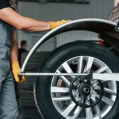 Mechanik w żółtych rękawiczkach ustawia koło na maszynie. Sprawdź wyważanie kół cena i zadbaj o bezpieczeństwo jazdy.