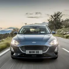 Ciemny Ford Focus MK5 jedzie krętą drogą wśród gór. Słońce zachodzi, tworząc piękne światło.