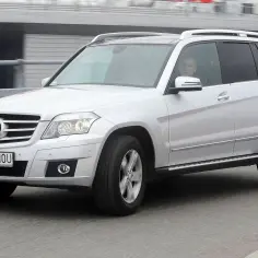 Srebrny Mercedes GLK w ruchu. Kierowca w okularach, widoczny przez szybę. Wiele osób szuka mercedes glk opinie przed zakupem.