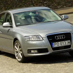 Srebrne Audi C6 z polskimi tablicami rejestracyjnymi PO 013JW jedzie po brukowanej drodze.