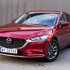 Czerwona Mazda 6 2.0 benzyna zaparkowana na kostce brukowej, z szarym murem w tle.