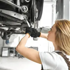 Mechaniczka z kluczem przy wahaczu. Sprawdza, jaka będzie wymiana wahacza cena.