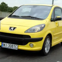 Żółty Peugeot 1007 z przesuwnymi drzwiami jedzie po drodze.