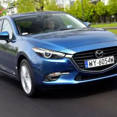 Niebieska Mazda 3 BL jedzie po drodze, za kierownicą siedzi mężczyzna.