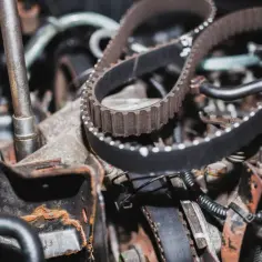Mechanik przygotowuje wymianę paska rozrządu w silniku samochodowym. Widoczny jest nowy, zębaty pasek i narzędzia.