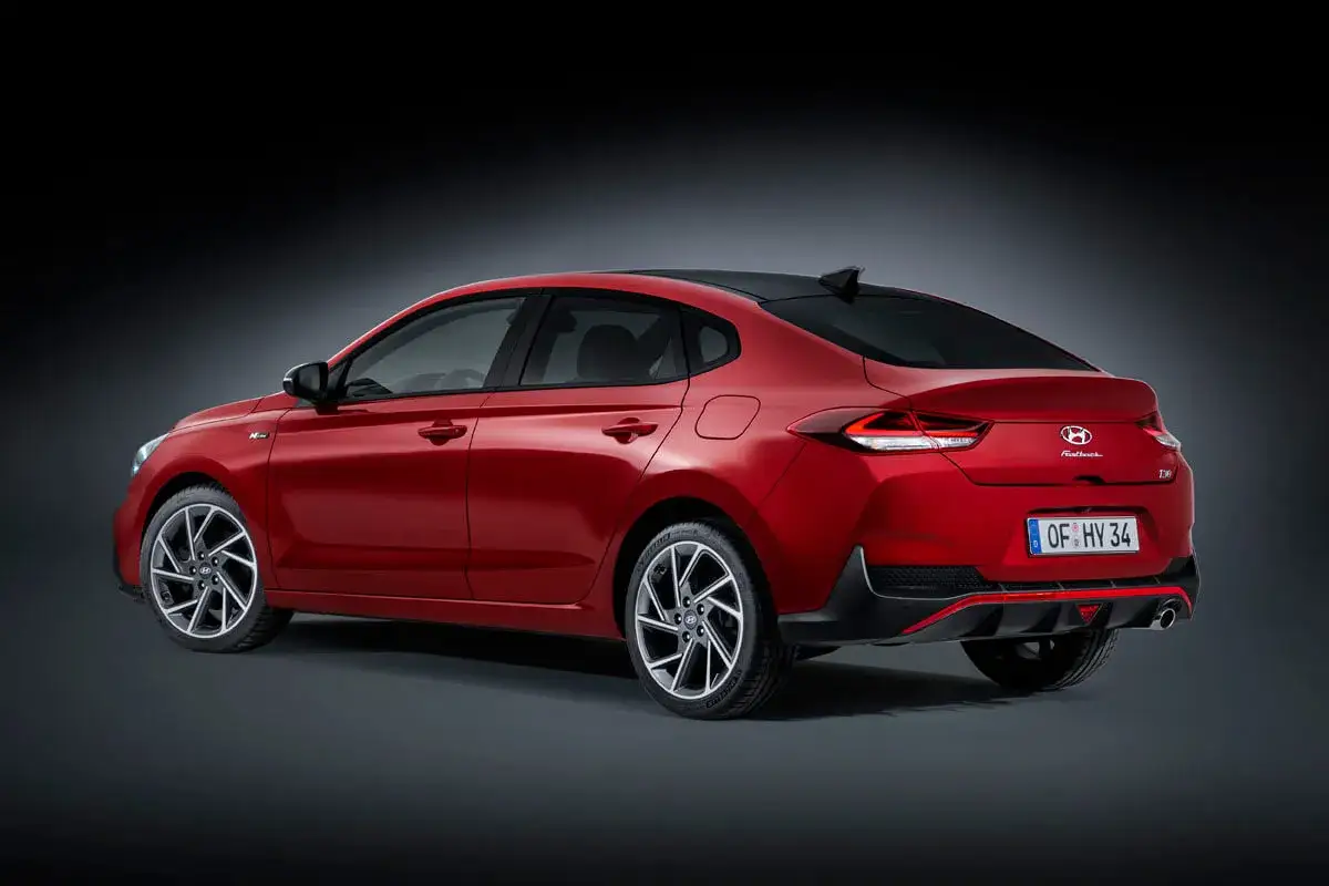 Czerwony Hyundai i30 Fastback z czarnym dachem i felgami, prezentujący sportowy design.
