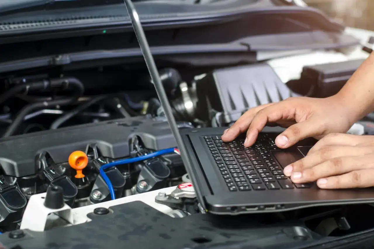 Mechanik diagnozuje usterkę silnika, sprawdzając dane na laptopie. Może to być problem z zapłonem lub nawet zasygnalizowany przez kierunkowskaz błąd.