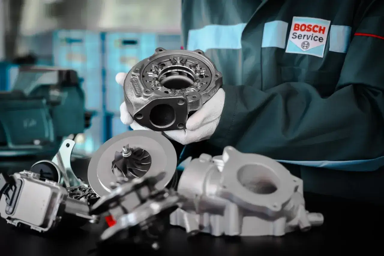 Mechanik w białych rękawiczkach prezentuje turbosprężarkę, kluczowy element silnika, który pomaga w prawidłowym działaniu odmy olejowej.
