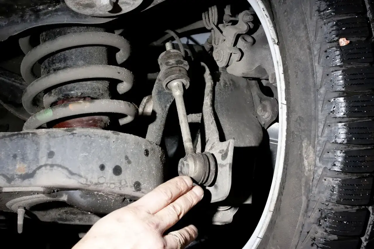 Dłoń mechanika wskazuje na zużyty łącznik stabilizatora, jeden z objawów problemów z zawieszeniem.