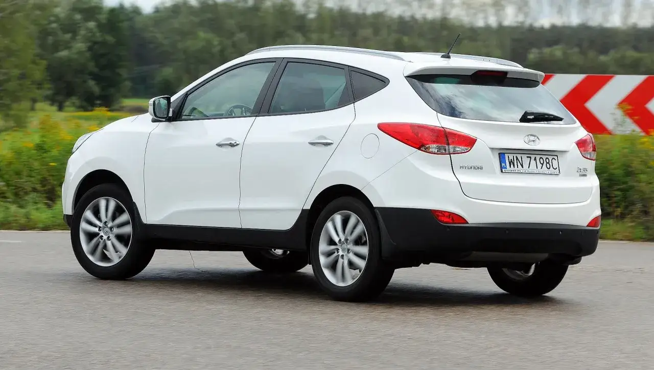 Biały Hyundai ix35 w ruchu, z widocznymi światłami i tablicą rejestracyjną. Wiele pozytywnych hyundai ix35 opinie potwierdza jego wszechstronność.