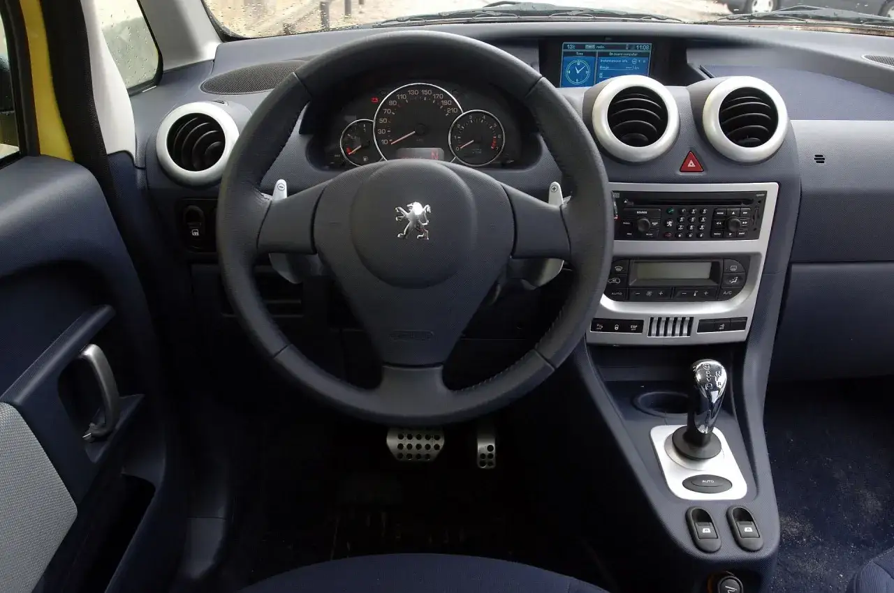 Wnętrze Peugeot 1007 z kierownicą, deską rozdzielczą i dźwignią zmiany biegów.