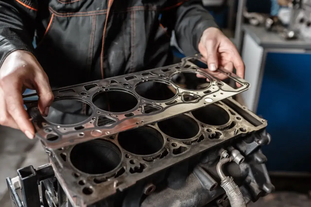 Mechanik trzyma nową uszczelkę pod głowicą, gotową do montażu na bloku silnika.