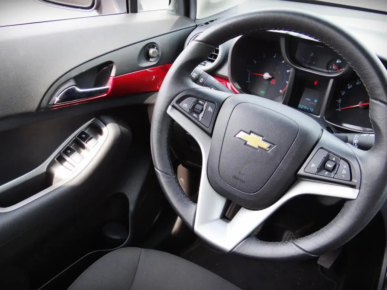 Wnętrze Chevrolet Orlando, kierownica z przyciskami i logo, panel drzwi z podnośnikami szyb. Wiele osób szuka chevrolet orlando opinie.