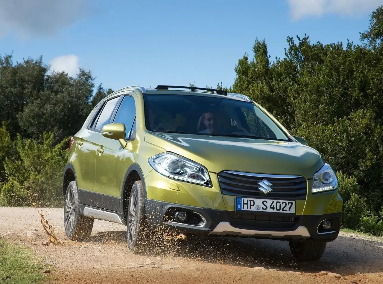 Zielony Suzuki SX4 S-Cross pokonuje teren, wzbijając kurz. Czy to jego wady?