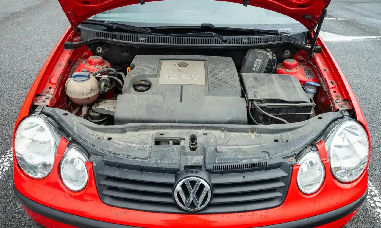 Otwarta maska czerwonego VW Polo 1.2 benzyna. Widoczny silnik i elementy komory silnika.