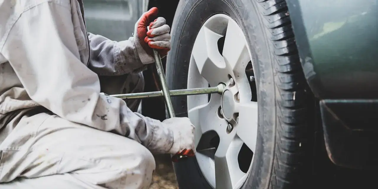 Mechanik w rękawiczkach dokręca śruby koła kluczem. Szybka wymiana opon to klucz do bezpieczeństwa.