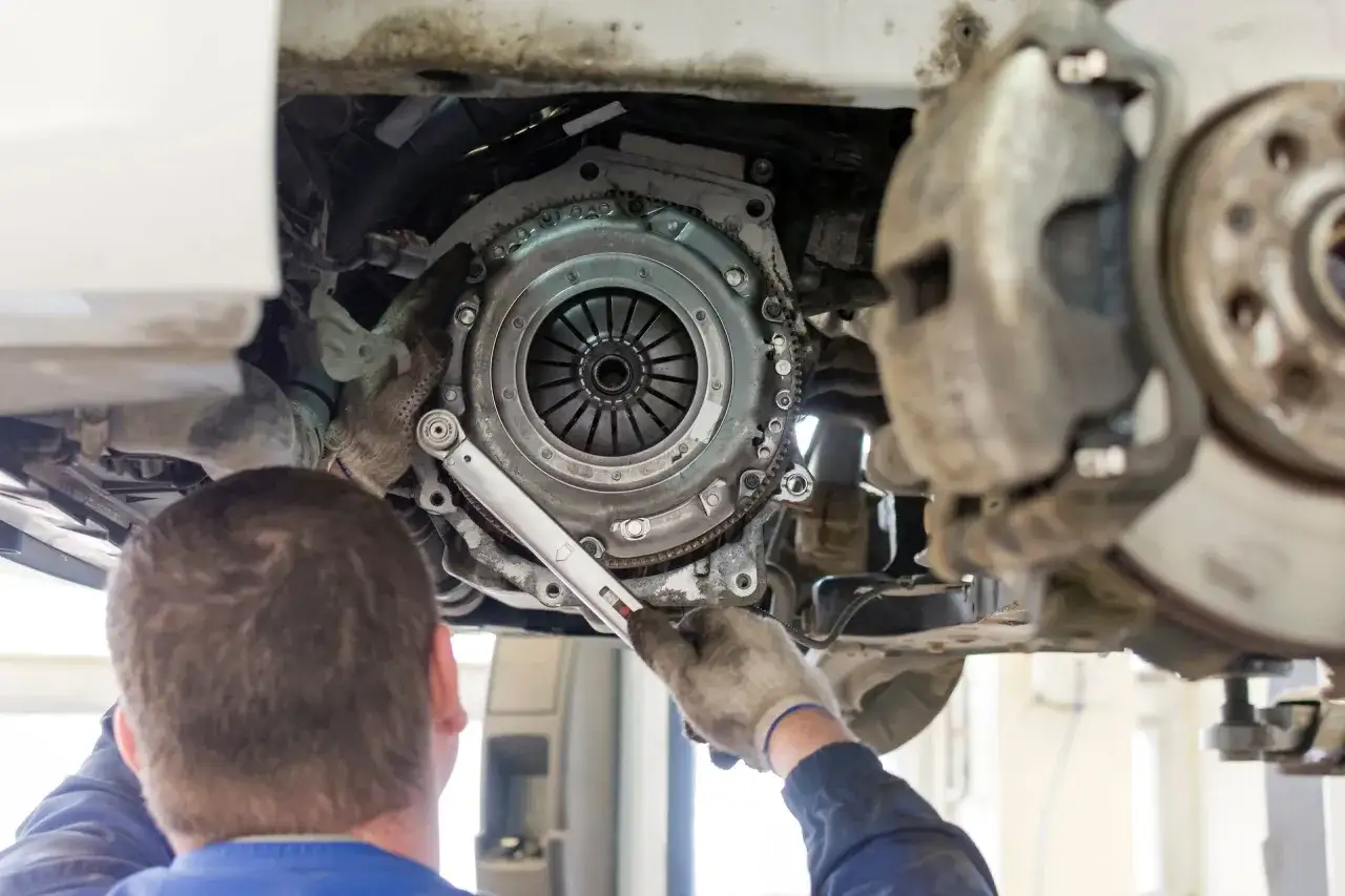 Mechanik dokręca śruby koła zamachowego. Wymiana sprzęgła kosztuje, ale jest konieczna dla sprawnego działania auta.