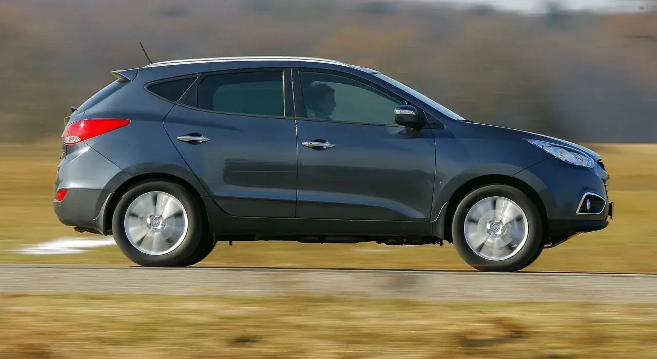 Szary Hyundai ix35 w ruchu. Kierowca w środku, za nim rozmyte tło. Wiele pozytywnych hyundai ix35 opinie potwierdza jego wszechstronność.